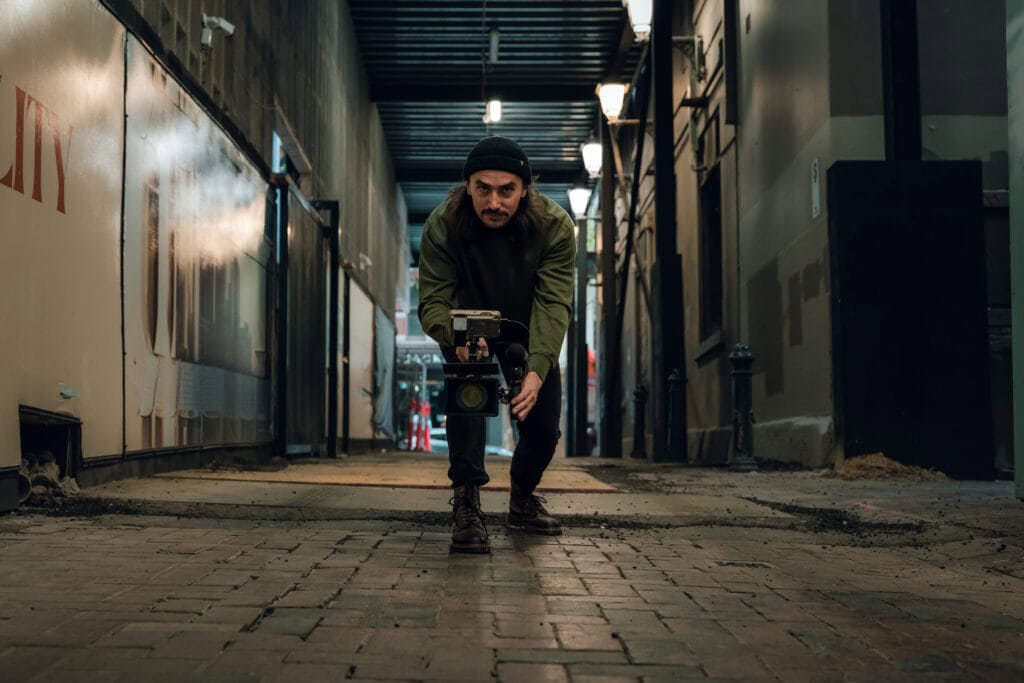 Man operating a professional camera on a city street at night.